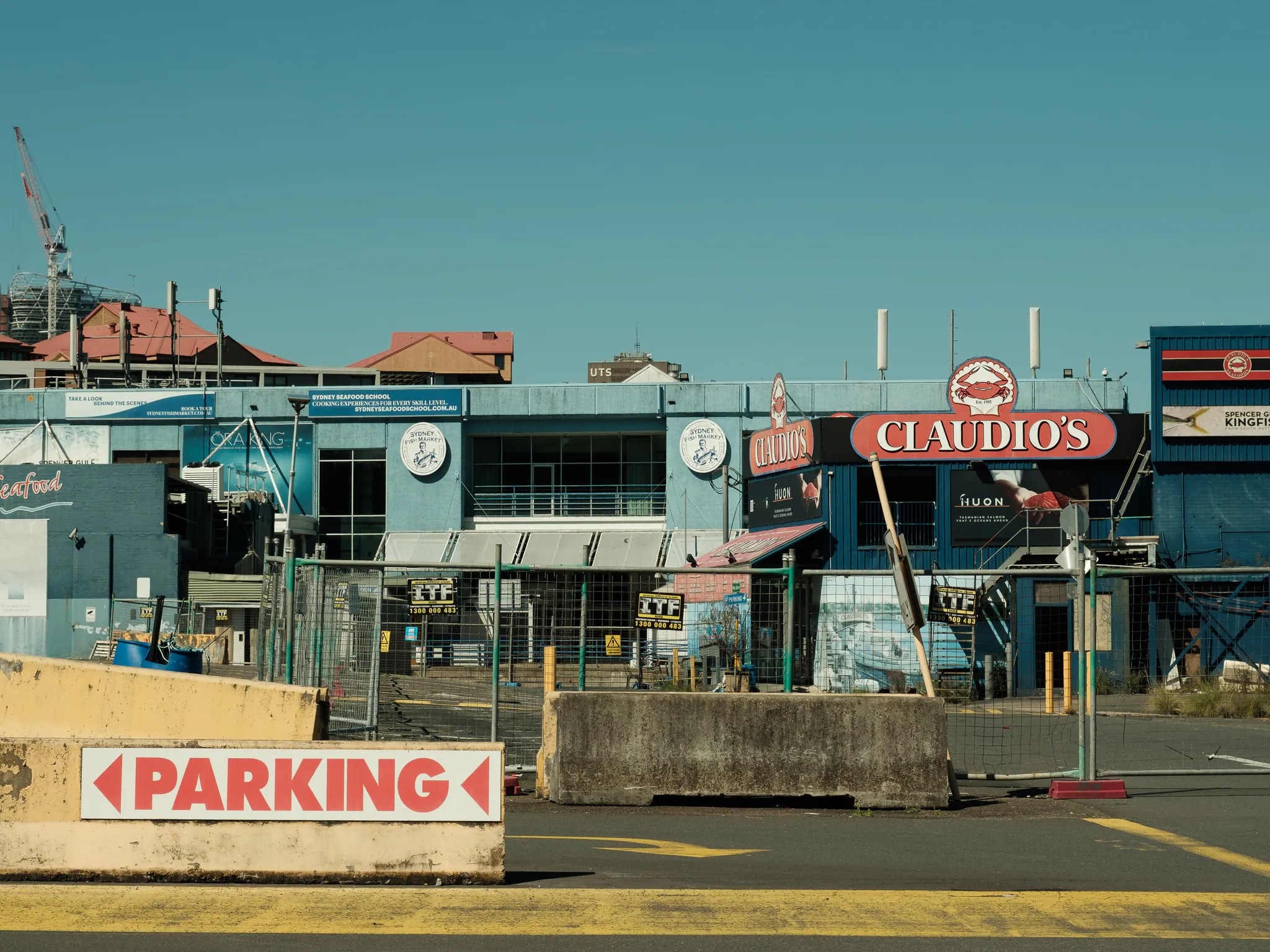 the fenced-off old sydney fish market, a red claudio’s sign behind an empty car park and a parking arrow on a concrete barrier