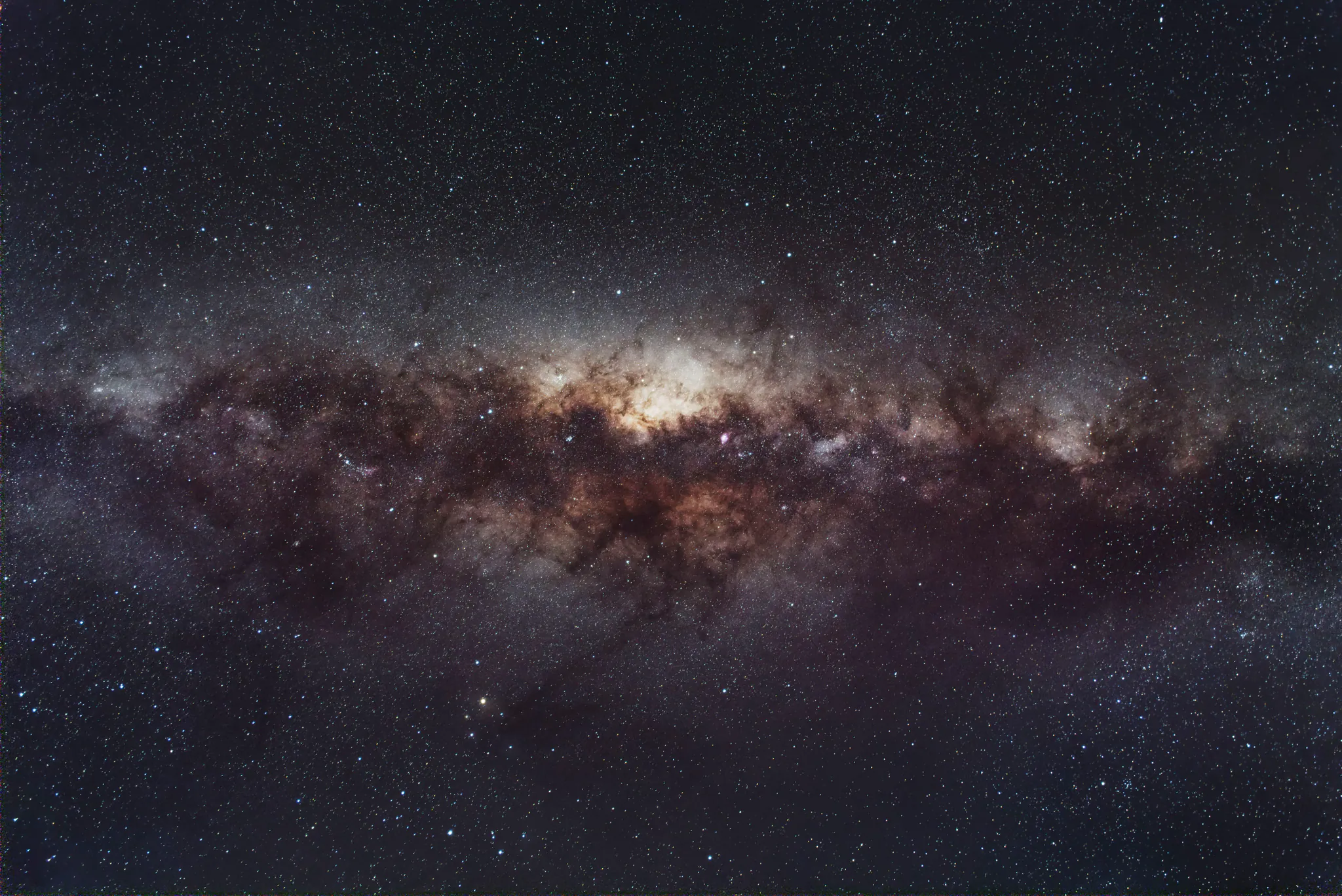 the core of the milky way stretched across a dark sky, dust lanes in rust and brown, dense fields of stars around it