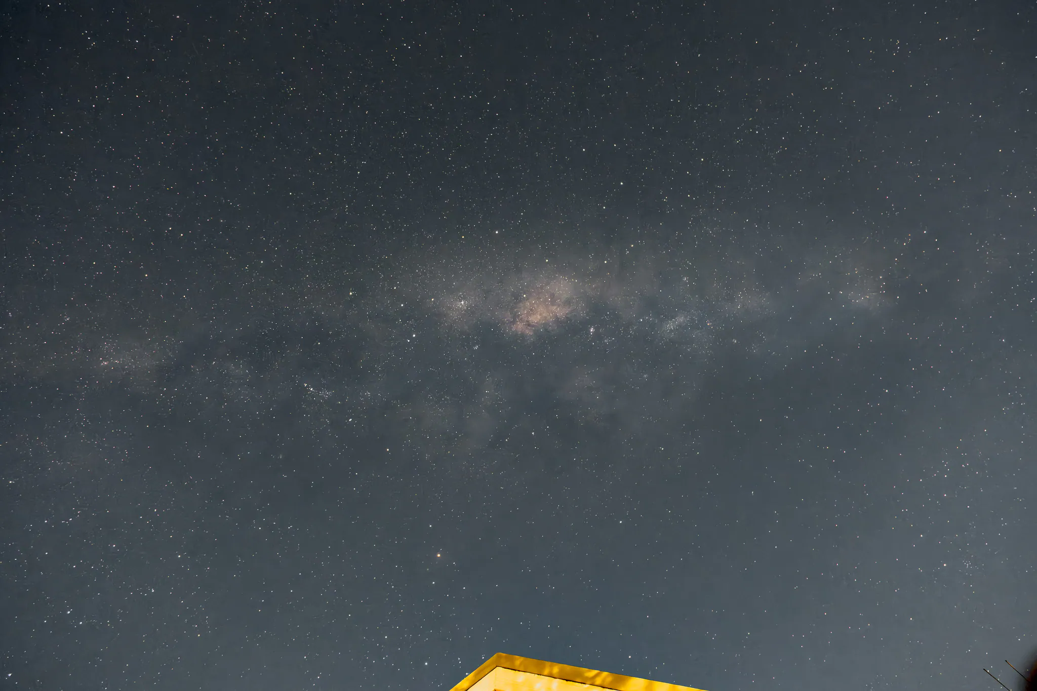 a faint milky way over a lit rooftop edge, grey sky full of noise and stars, before any processing