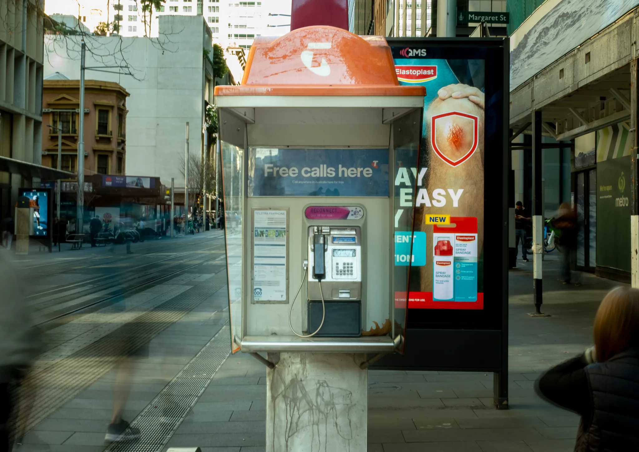 a payphone on margaret street standing in front of a bright bandaid billboard that competes for attention